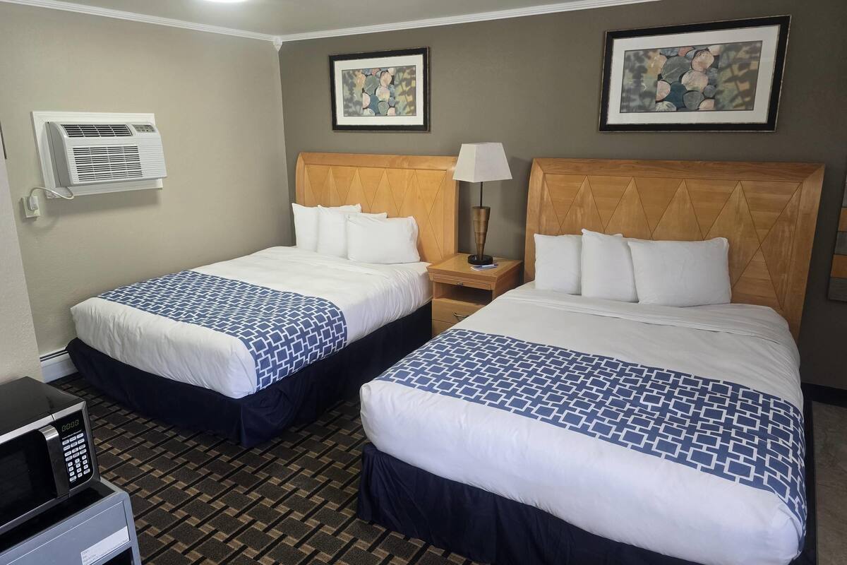 Two double beds with patterned bedspreads, a bedside table with a lamp, an air conditioning unit, and a microwave.