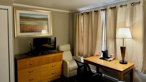 Una habitación de hotel con escritorio, silla, televisor y un cuadro en la pared.