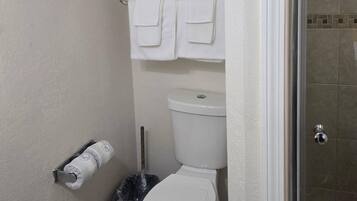A bathroom with a toilet, a towel rack with two towels, a toilet paper holder, and a trash bin.