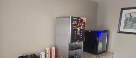 Une machine à café ornée d’une publicité Nescafe, un mousseur à lait et un distributeur de café, le tout posé sur un comptoir en granit dans une chambre d’hôtel.