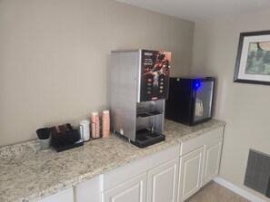 Une machine à café ornée d’une publicité Nescafe, un mousseur à lait et un distributeur de café, le tout posé sur un comptoir en granit dans une chambre d’hôtel.