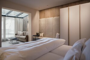 A modern hotel room with a large bed, a seating area with a sofa and a small table, and a large window with curtains.