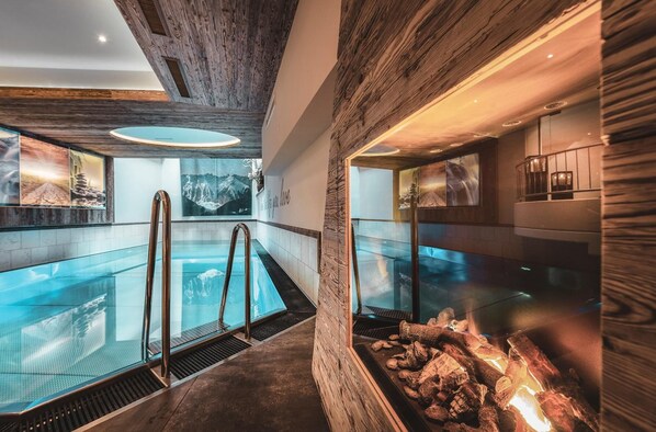 Un espace piscine intérieur moderne, doté d’une paroi en verre, d’éléments décoratifs en bois et d’une cheminée.