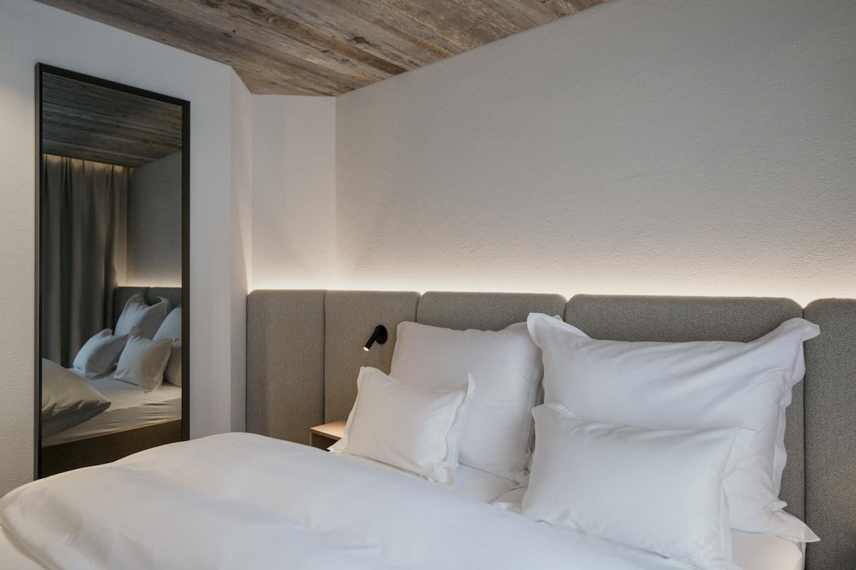 A modern bedroom with a large bed, a nightstand, a mirror, and a headboard.