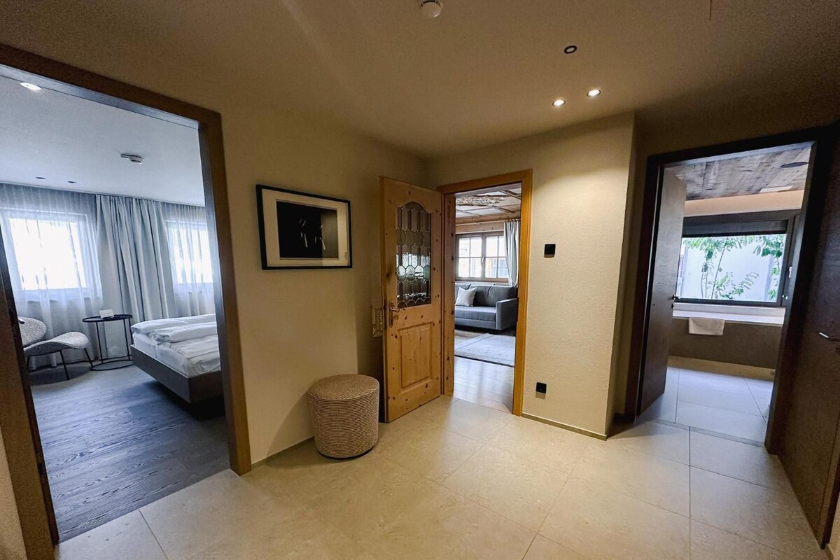 Habitación de hotel con una cama, una mesita redonda pequeña, una silla, una puerta con panel de vidrio y vistas a un balcón.