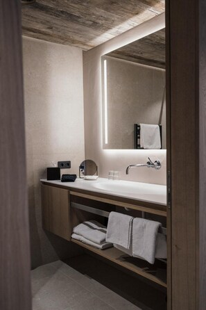 A modern bathroom with a large mirror, a white sink, and a wooden vanity.