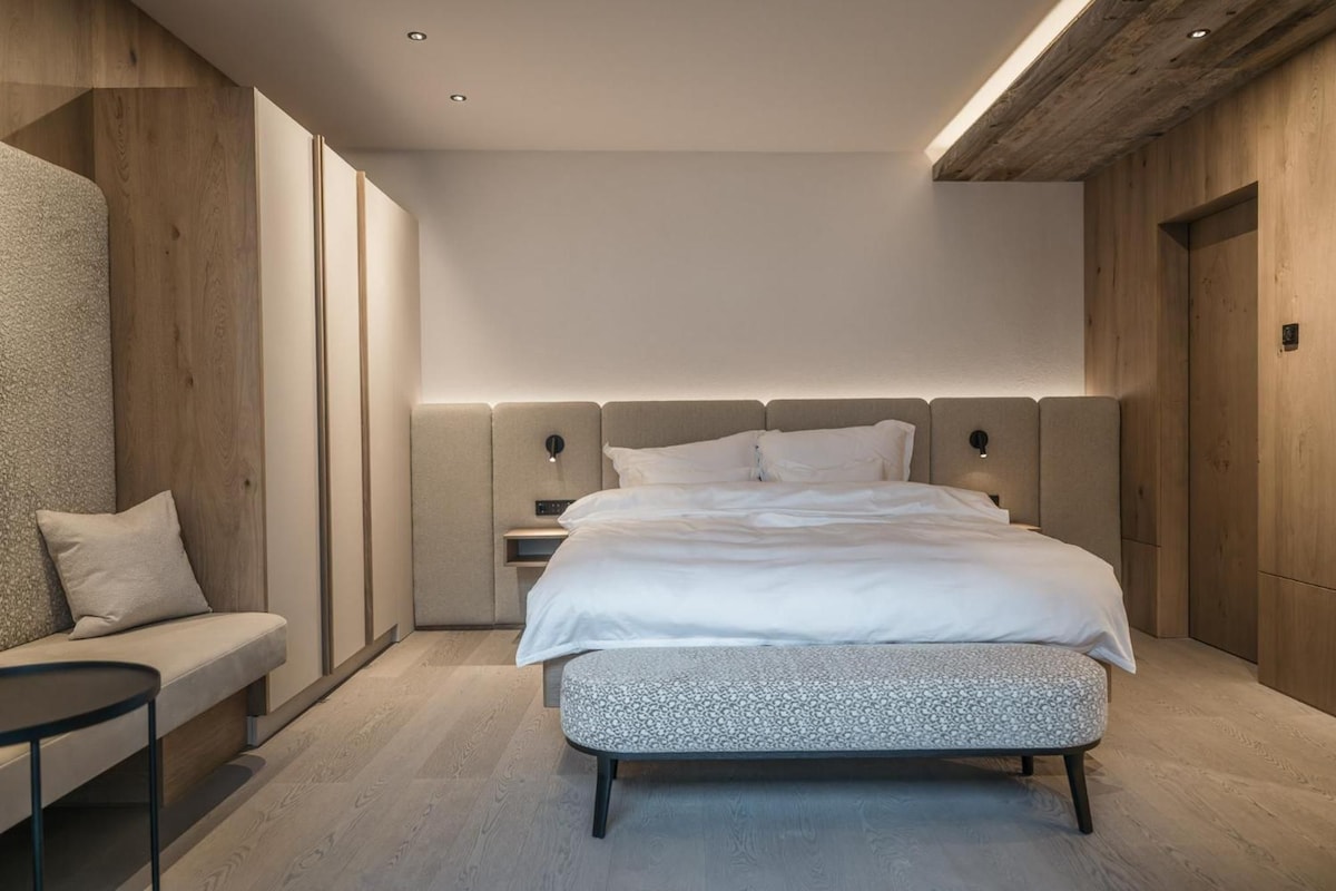 Un dormitorio moderno con una cama grande, mesitas de noche, un banco y techo de madera.
