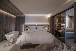 A modern hotel room with a large bed, a bathtub, and a glass-enclosed seating area.