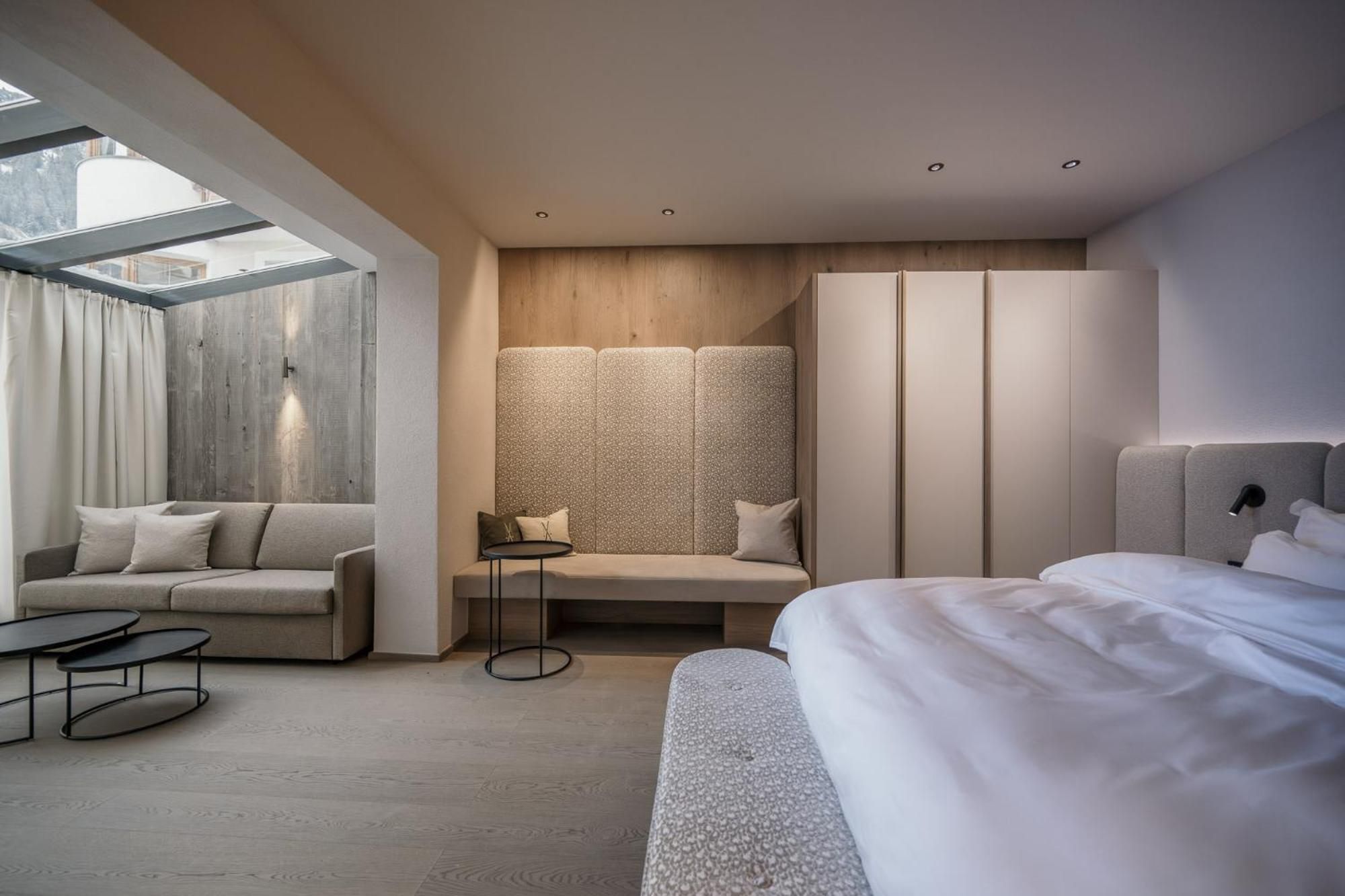 A modern hotel room with a bed, a sofa, a small table, and a seating area with a patterned wall.