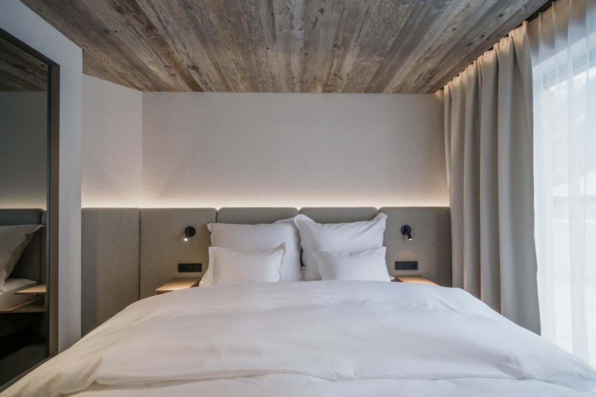 Habitación de hotel moderna con una cama grande, techo de madera y vistas al exterior.