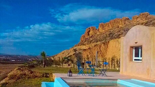 Zona de piscina con vistas a un promontorio rocoso y un edificio con ventana.