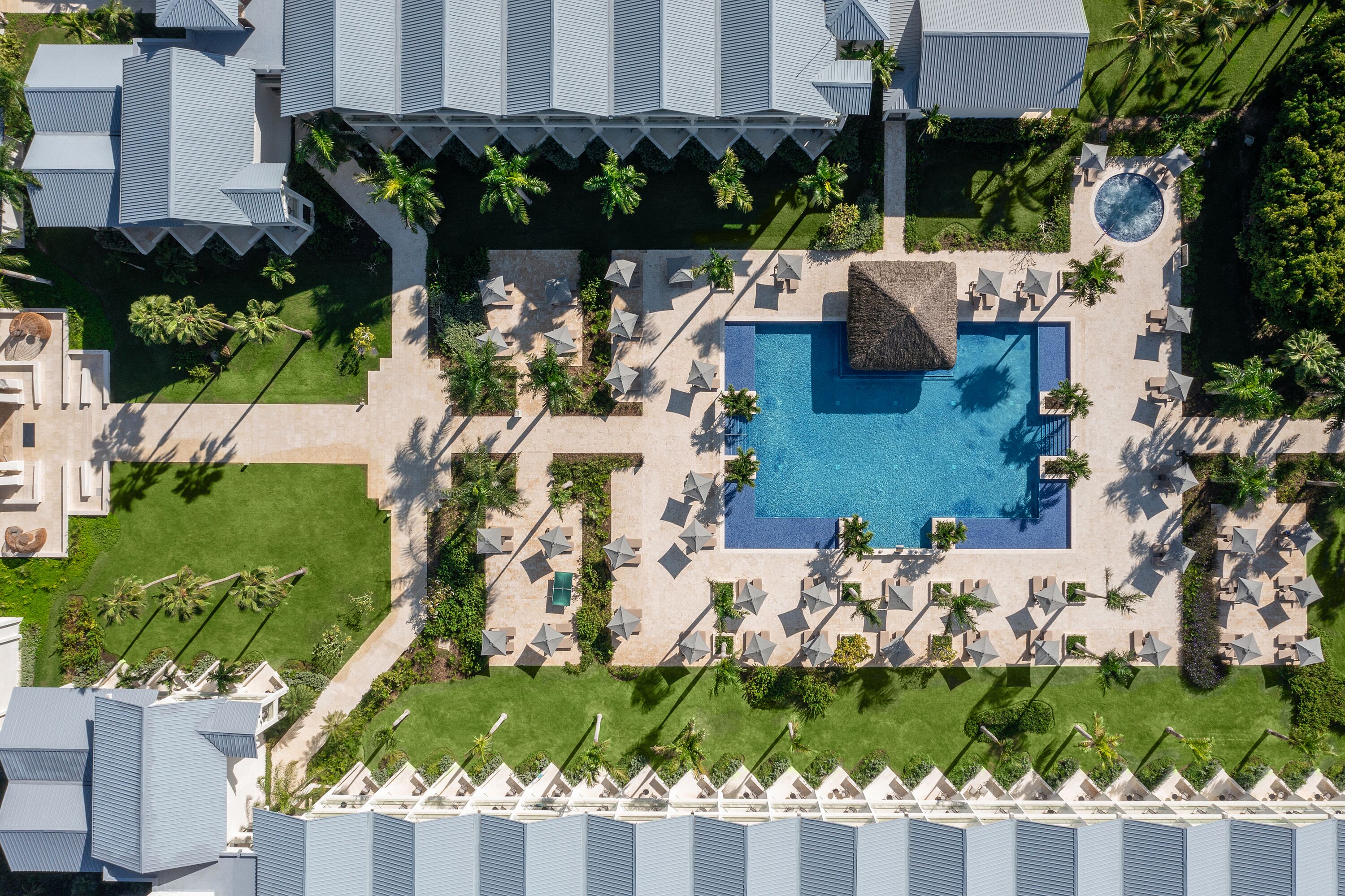 An aerial view of a resort with a central swimming pool, multiple lounge areas, and palm trees.