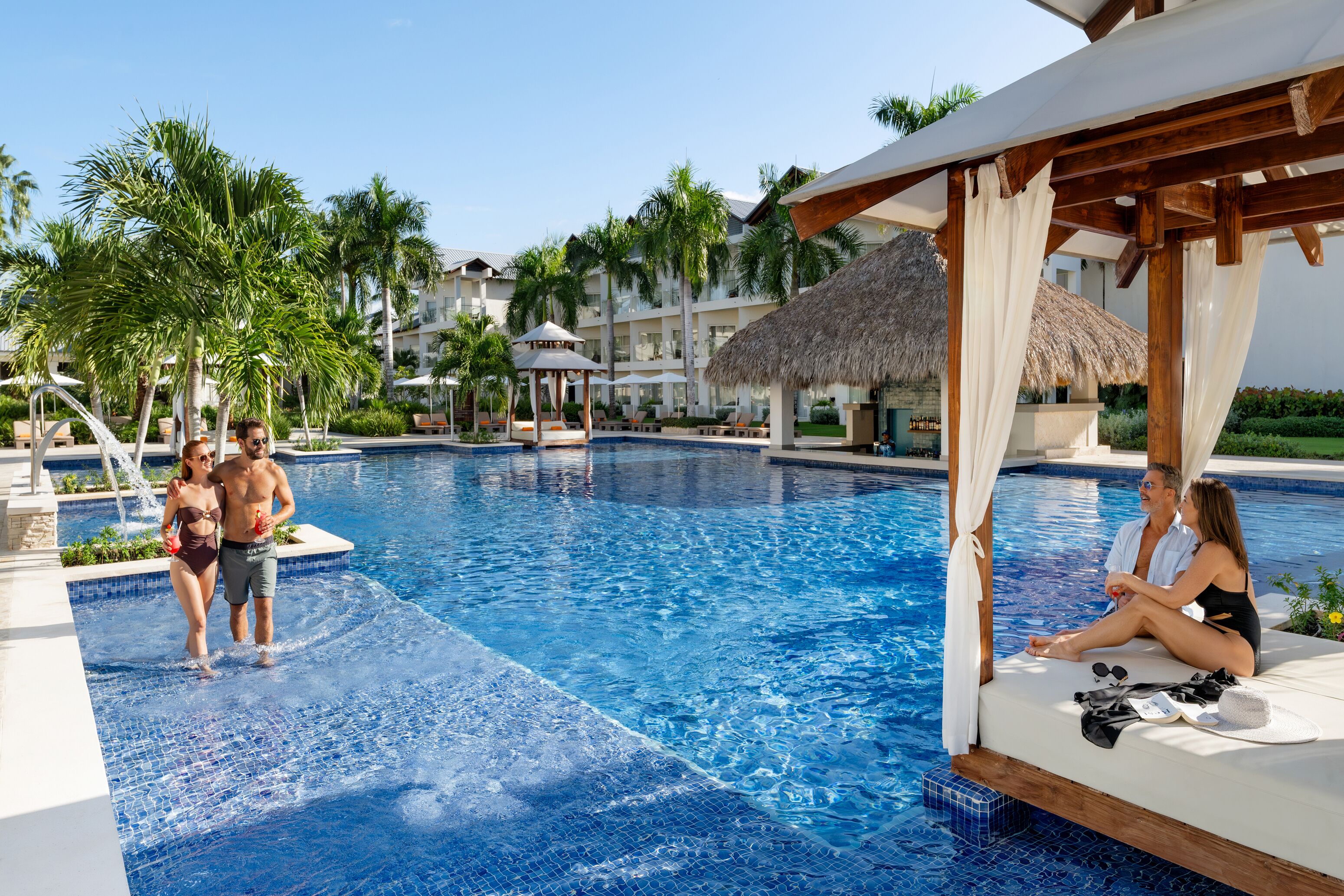 A swimming pool with a cabana, palm trees, and a thatched-roof structure.