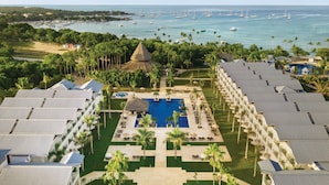 A resort with a central swimming pool, multiple guest rooms, and a view of the ocean with boats. - Secrets La Romana Resort & Spa  - Adults Only - All Inclusive (San Rafael del Yuma)