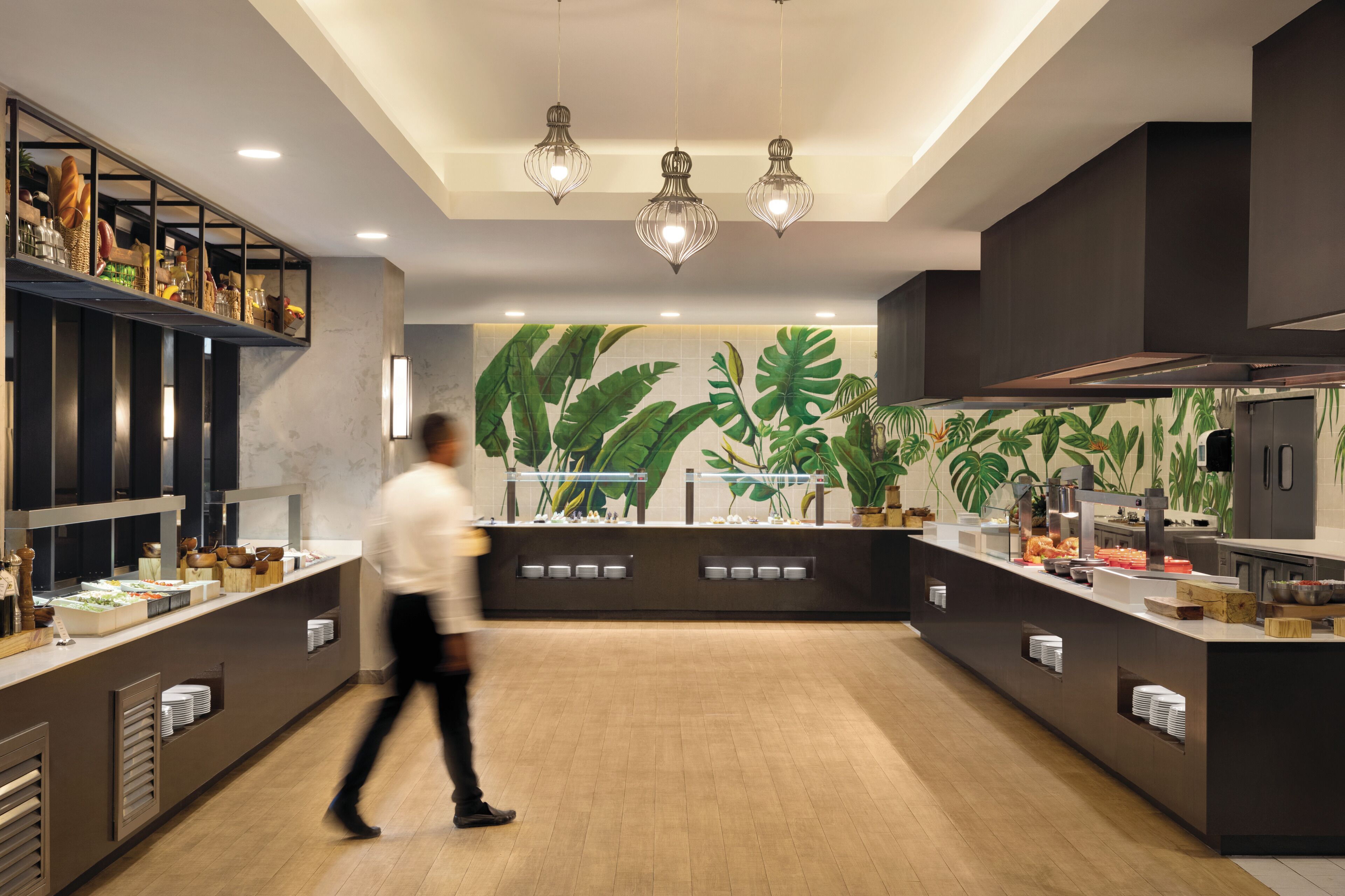 A modern kitchen with a central island, overhead lighting, and a tropical-themed wall mural.