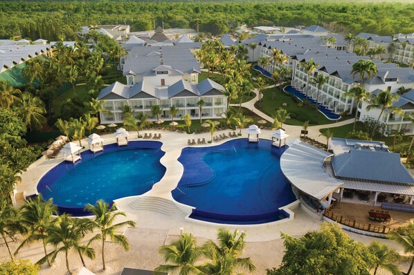 Un resort con dos piscinas amplias, palmeras y edificios del resort.