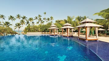 A clear blue pool with four gazebos, surrounded by palm trees and lounge chairs.