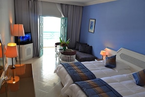 Habitación de hotel con cama, lámparas de noche, televisión, una mesita con planta y vistas al exterior.