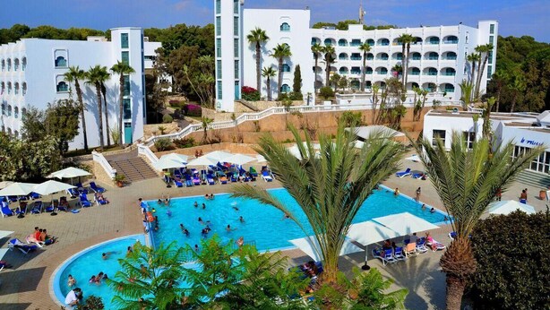 A resort with a large pool, multiple buildings, and palm trees. - Hotel Tivoli (Agadir)