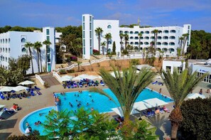 Un resort con una piscina grande, varias edificaciones y palmeras.
