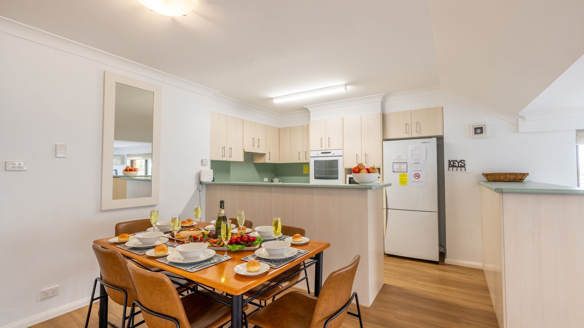 A modern kitchen with a dining area, featuring a wooden table set for a meal, a refrigerator, and a microwave.