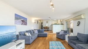 Ein modernes Wohnzimmer mit grauen Sofas, einem Flachbildfernseher und einem großen Gemälde mit einer Strandansicht.