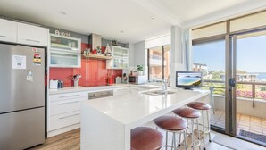 A modern kitchen with a large island, bar stools, and a view of the sea. - The Commodore, 23,9-11 Donald Street - Delightful unit with gorgeous water views, air con and wi-fi (Nelson Bay)