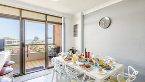 A dining area with a table set for four, a grill outside, and a view of the beach. - The Commodore, 23,9-11 Donald Street - Delightful unit with gorgeous water views, air con and wi-fi (Nelson Bay)