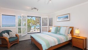 A bedroom with a bed, a chair, a nightstand, and a window with shutters. - Florentine, 12/11 Columbia Close - WIFI, Aircon, spectacular views (Nelson Bay)