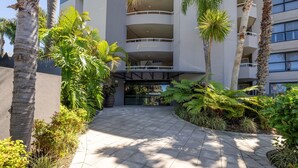 A hotel entrance with a covered walkway, palm trees, and a building with balconies. - Florentine, 12/11 Columbia Close - WIFI, Aircon, spectacular views (Nelson Bay)