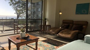 Ein Wohnzimmer mit einem Ledersofa, einem Holztisch und Blick auf einen Balkon mit Gartenmöbeln.