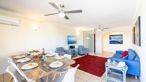 A dining area with a wooden table set for four, a red rug, and a blue sofa in the living area.