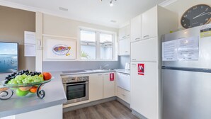 Eine moderne Küche mit einem Edelstahl-Kühlschrank, einem Herd und einem Spülbecken. Auf dem Kühlschrank liegt eine Brandschutzdecke, und an der Wand hängt eine Uhr.