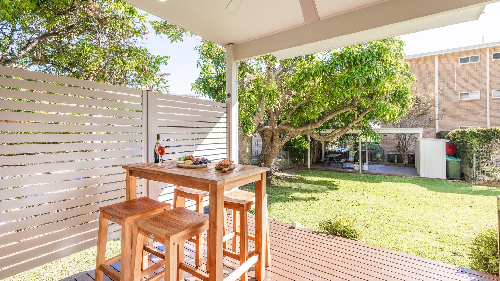 A wooden deck with a table and chairs, a pergola, and a tree.