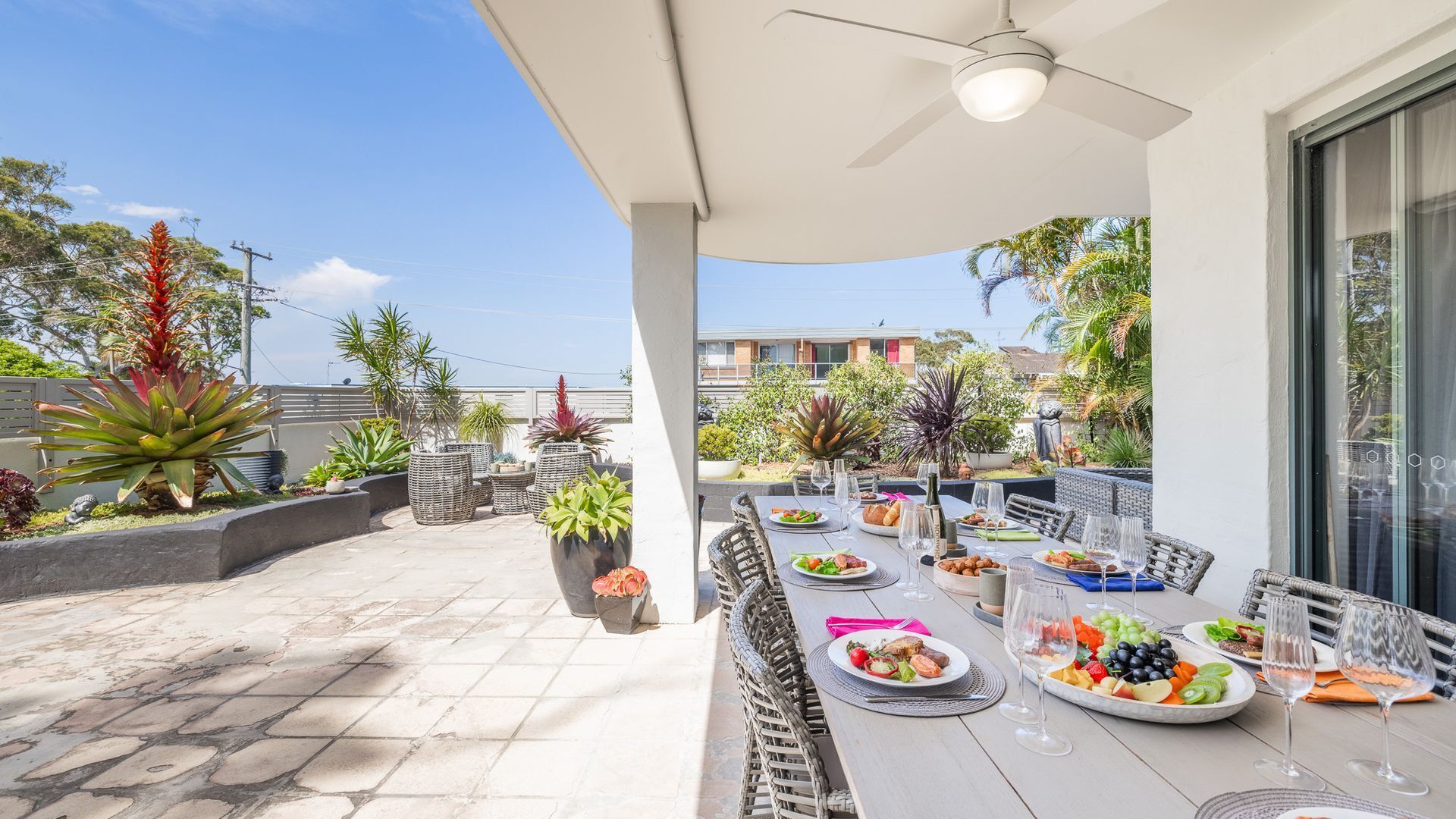 An outdoor patio with a long dining table, wicker chairs, and potted plants.