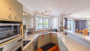 Una cocina compacta con estufa, horno y pileta, una ventana con persianas, y un comedor con sillas y una mesa.