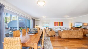 Amplia sala de estar con una mesa de comedor de madera, mobiliario de mimbre y un ventanal con vistas al exterior.