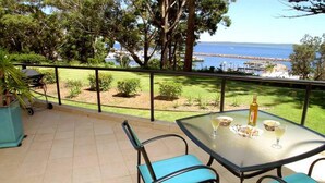 Un patio con una mesa para dos, una parrilla y vistas al mar y un puerto deportivo.