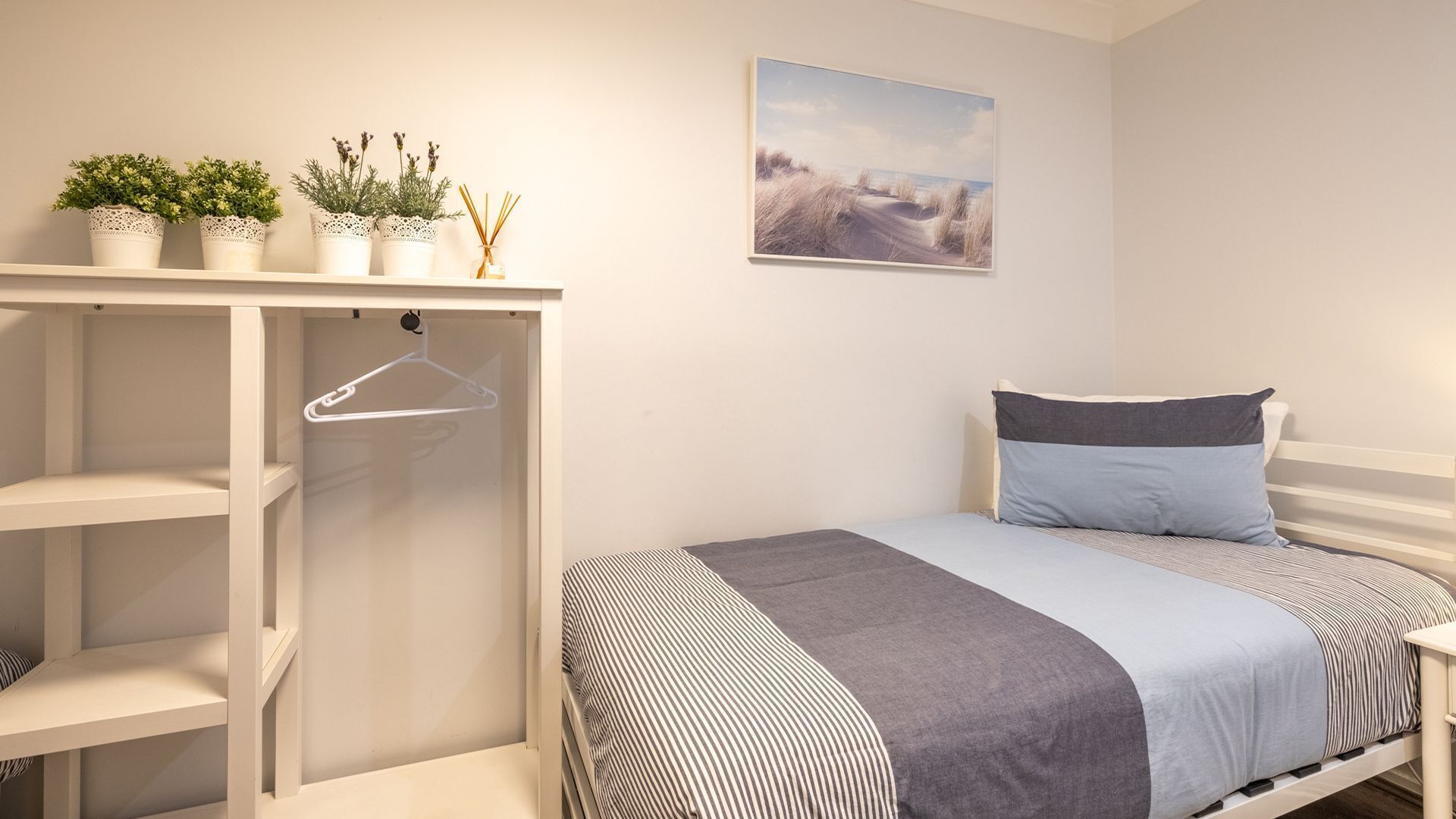 A bedroom with a bed, a hanging wardrobe, and a painting on the wall.