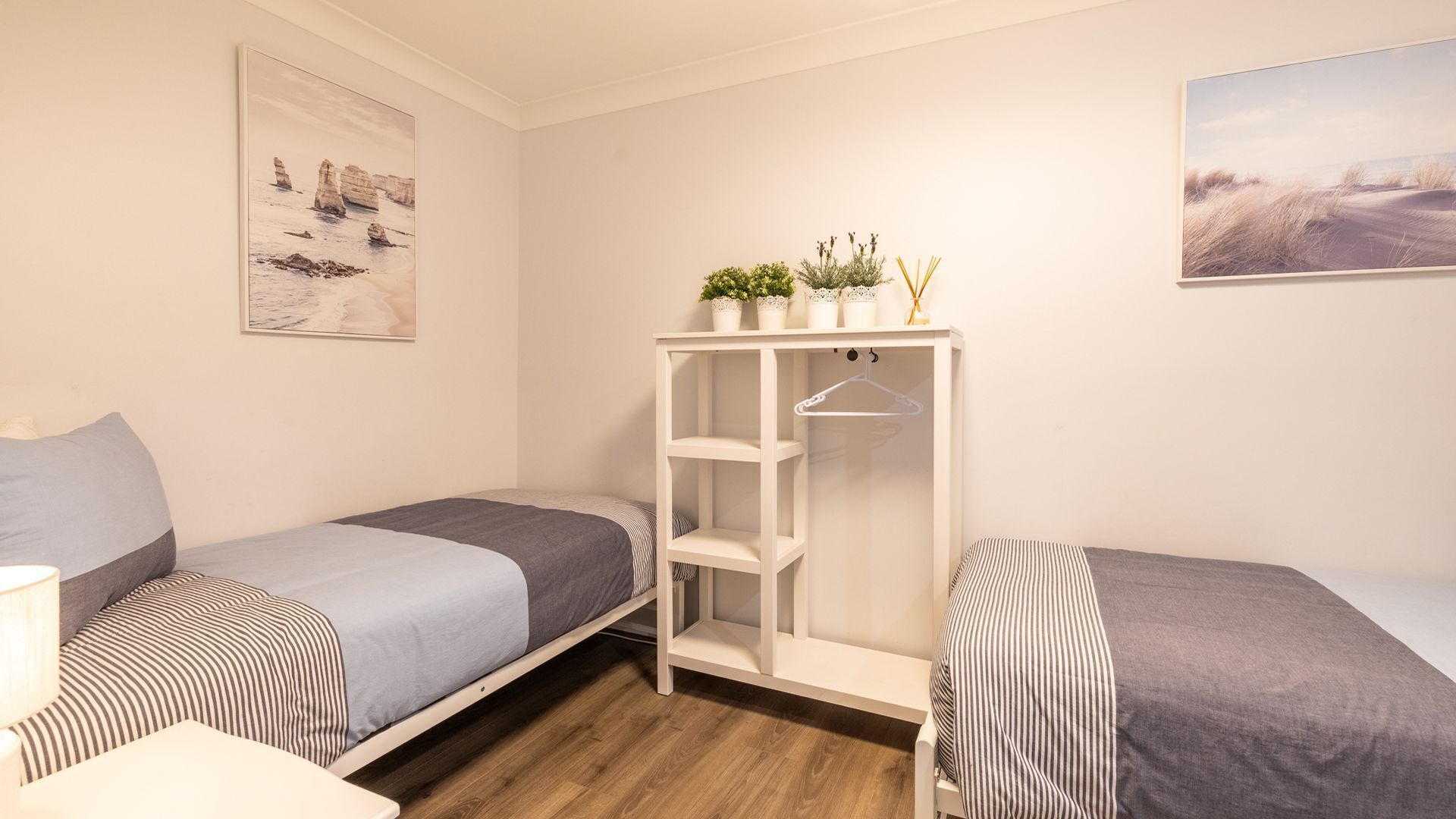 A bedroom with two single beds, a white wardrobe, and a painting on the wall.