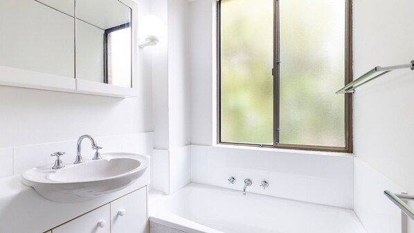 A modern bathroom with a white sink, a bathtub, and a frosted window. - Harbourside, 15/3-7 Soldiers Point Road - right on the waterfront (Soldiers Point)