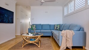 Una sala moderna con un sofá azul, una mesa de centro de vidrio y un ventilador de techo.