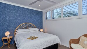 Un dormitorio con cama, ventana, ventilador de techo y mesita de noche.