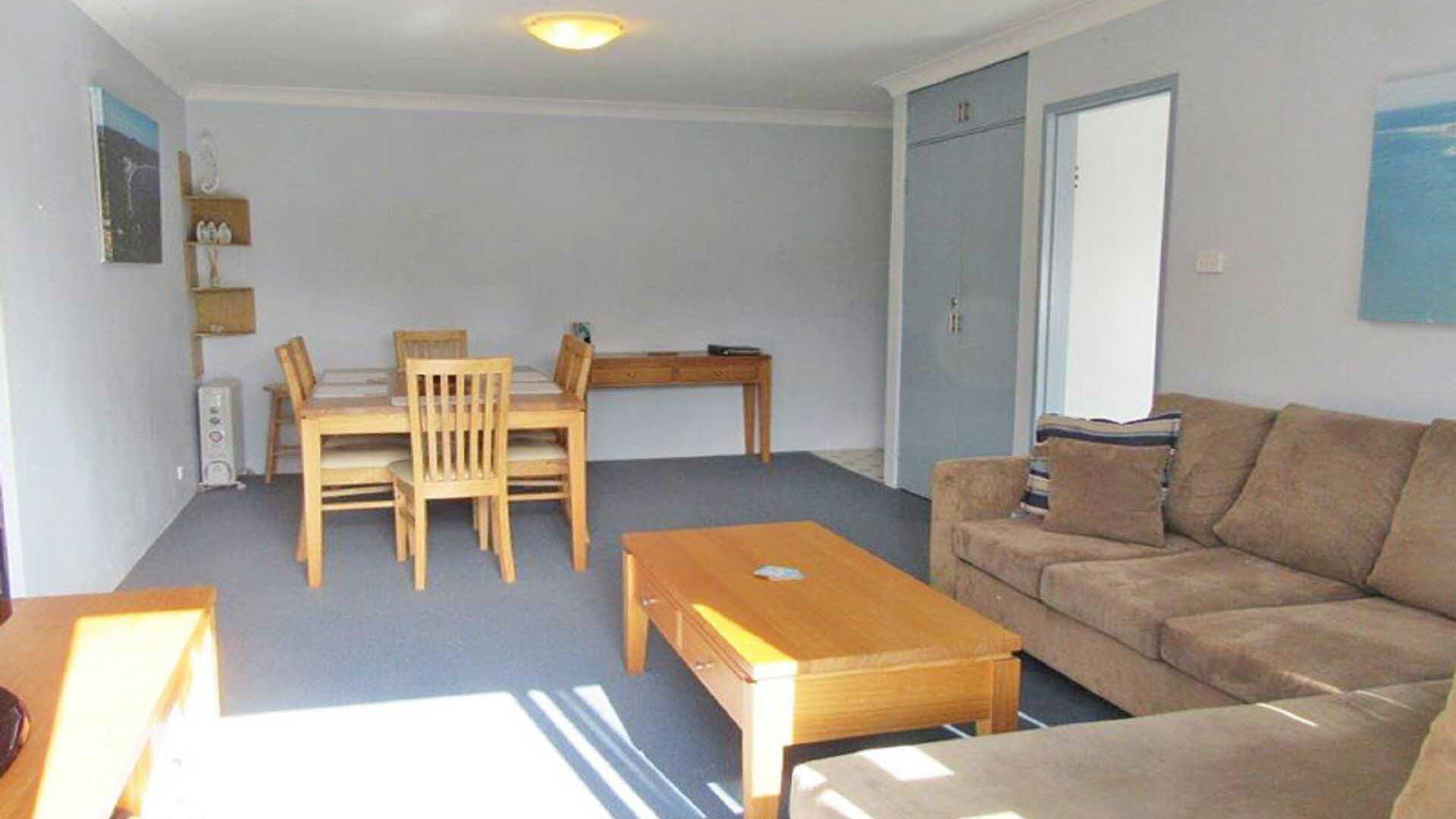 Ein Wohnzimmer mit Esstisch aus Holz, vier Stühlen, einem Sofa und einem Couchtisch.