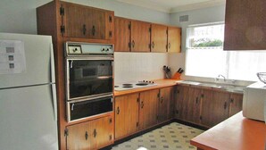 Une cuisine compacte avec des meubles en bois, un four encastré, un évier et une fenêtre qui laisse entrer la lumière naturelle.