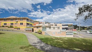 Um edifício residencial de vários andares com fachada de tijolo, uma linha de segurança amarela e um pequeno jardim frontal.