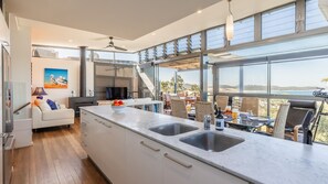 A modern kitchen with a large island, a dining area with outdoor seating, and a view of the ocean. - Beach House 7,  Air Conditioned, Wi-Fi, Foxtel, Linen, Communal Pool and Spa (One Mile)