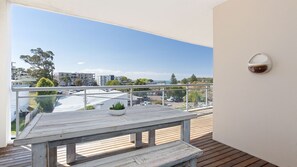 Un balcón con una mesa de madera y una planta en maceta, con vista a un estacionamiento y edificios.