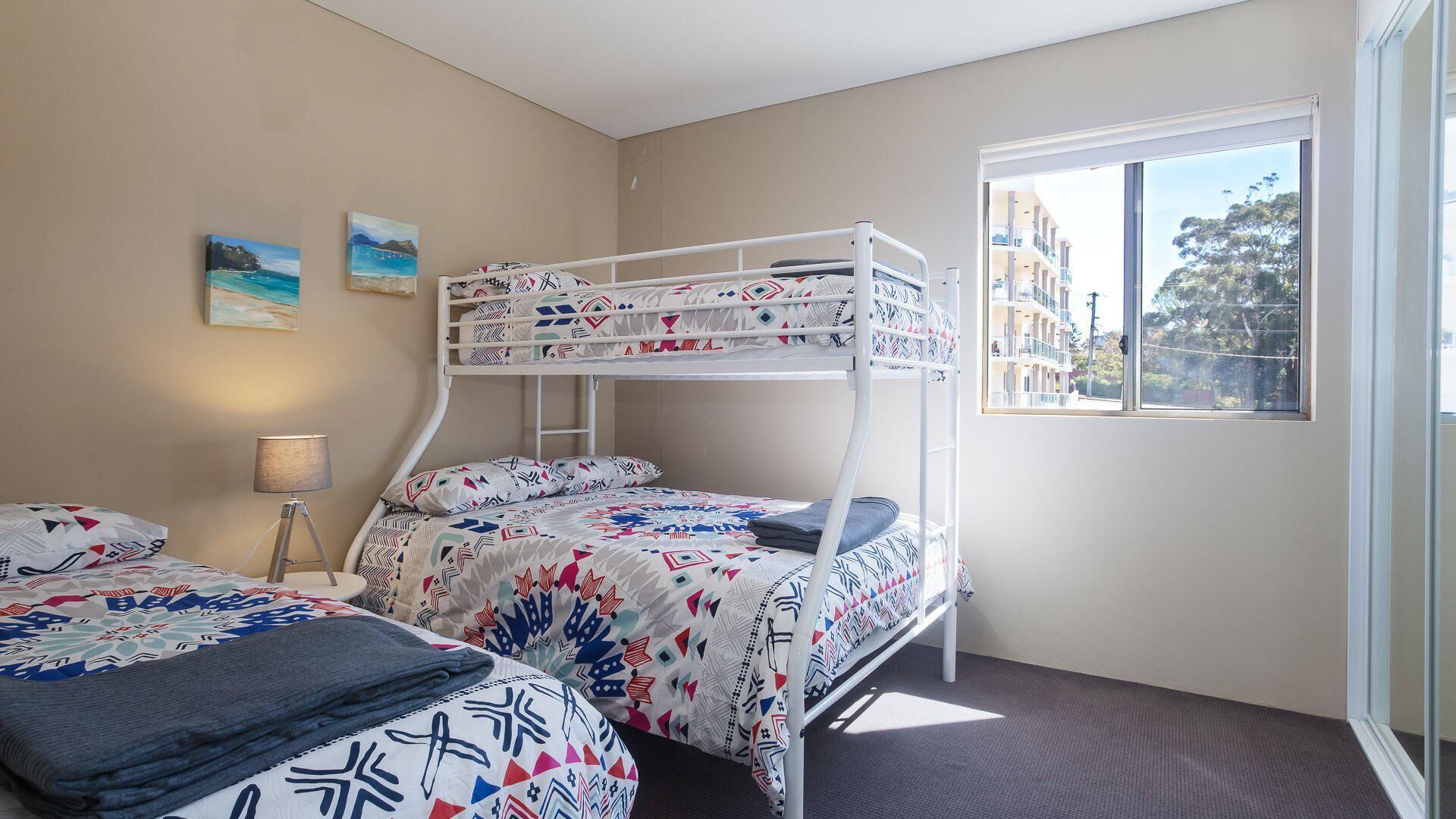 Habitación con literas, una ventana, una lámpara y dos cuadros en la pared.
