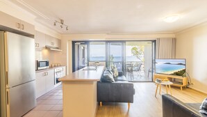 A modern kitchen with a refrigerator, microwave, and stove, leading to a balcony with a view of the sea. - Florentine, 7 11 Columbia Close - wifi, air conditioned unit with fantastic views of Little Beach (Nelson Bay)